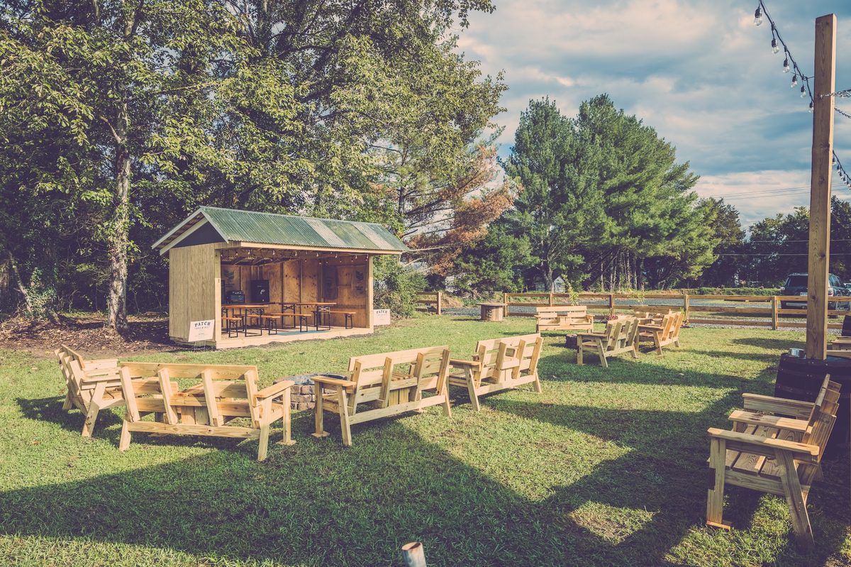 Timber glider benches around a fire ring on the lawn, a small open shed with a Patch sign behind