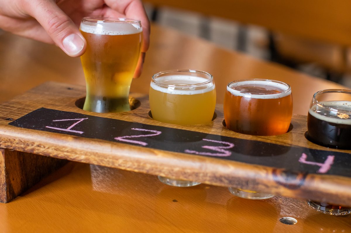 A hand lifting the first glass from a four-glass tasting flight on a wooden paddle chalked 1 to 4