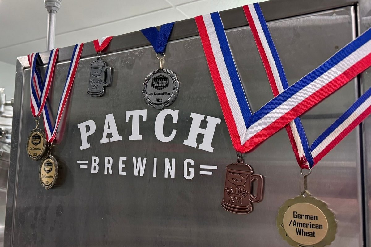The Patch Brewing logo on a stainless steel panel draped with competition medals